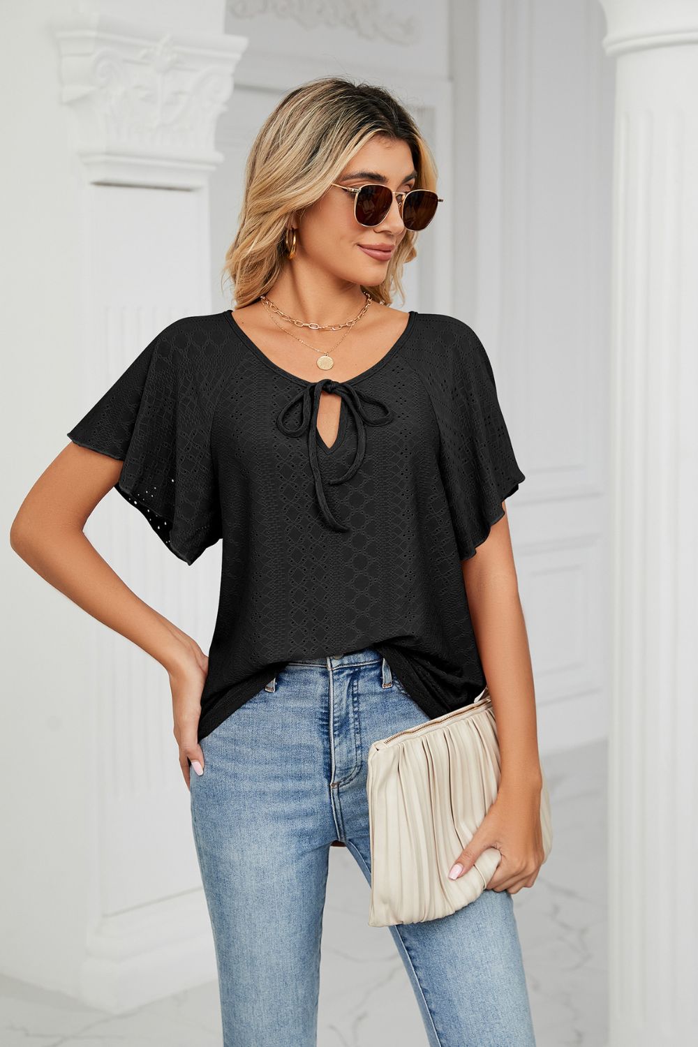 Black tie-neck flutter sleeve blouse front view with sunglasses and clutch