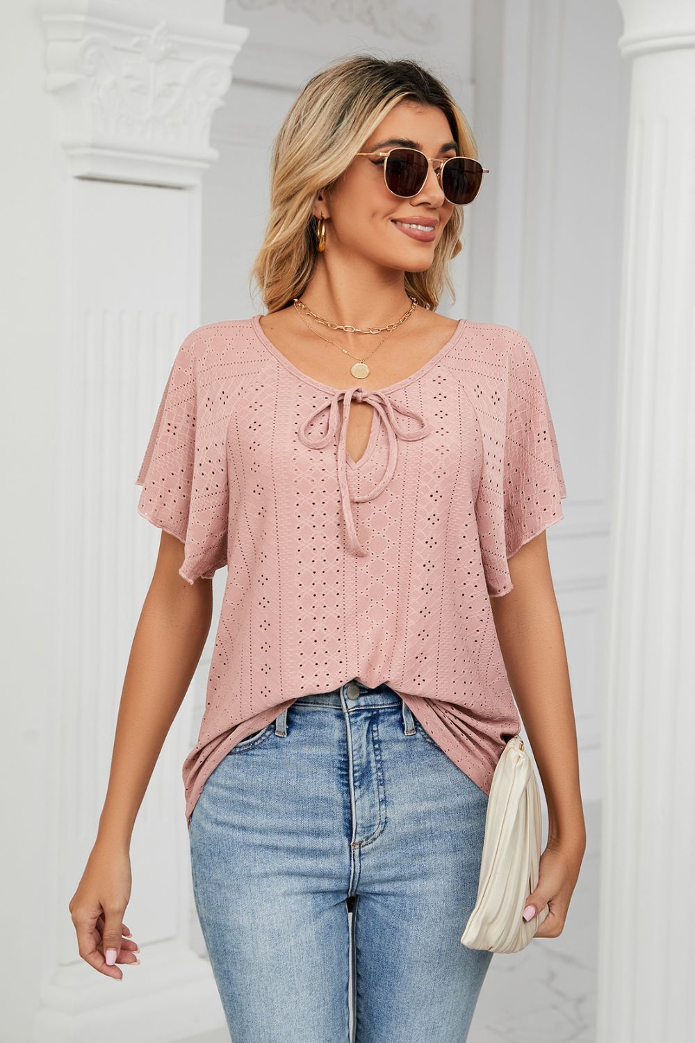 Pink eyelet tie-neck flutter sleeve blouse front view with sunglasses and purse